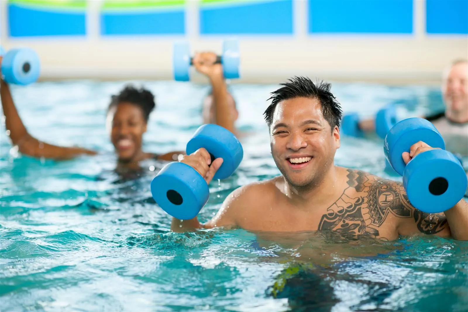 A man lifting weights and smiling during a pool workout.