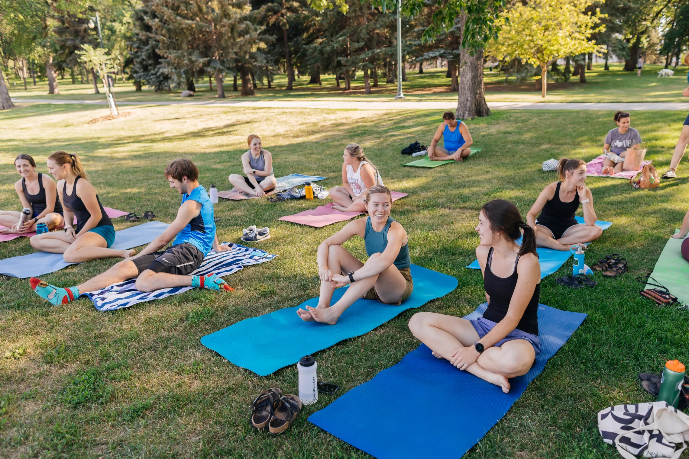 Friends smile and laugh as they do yoga in a park.