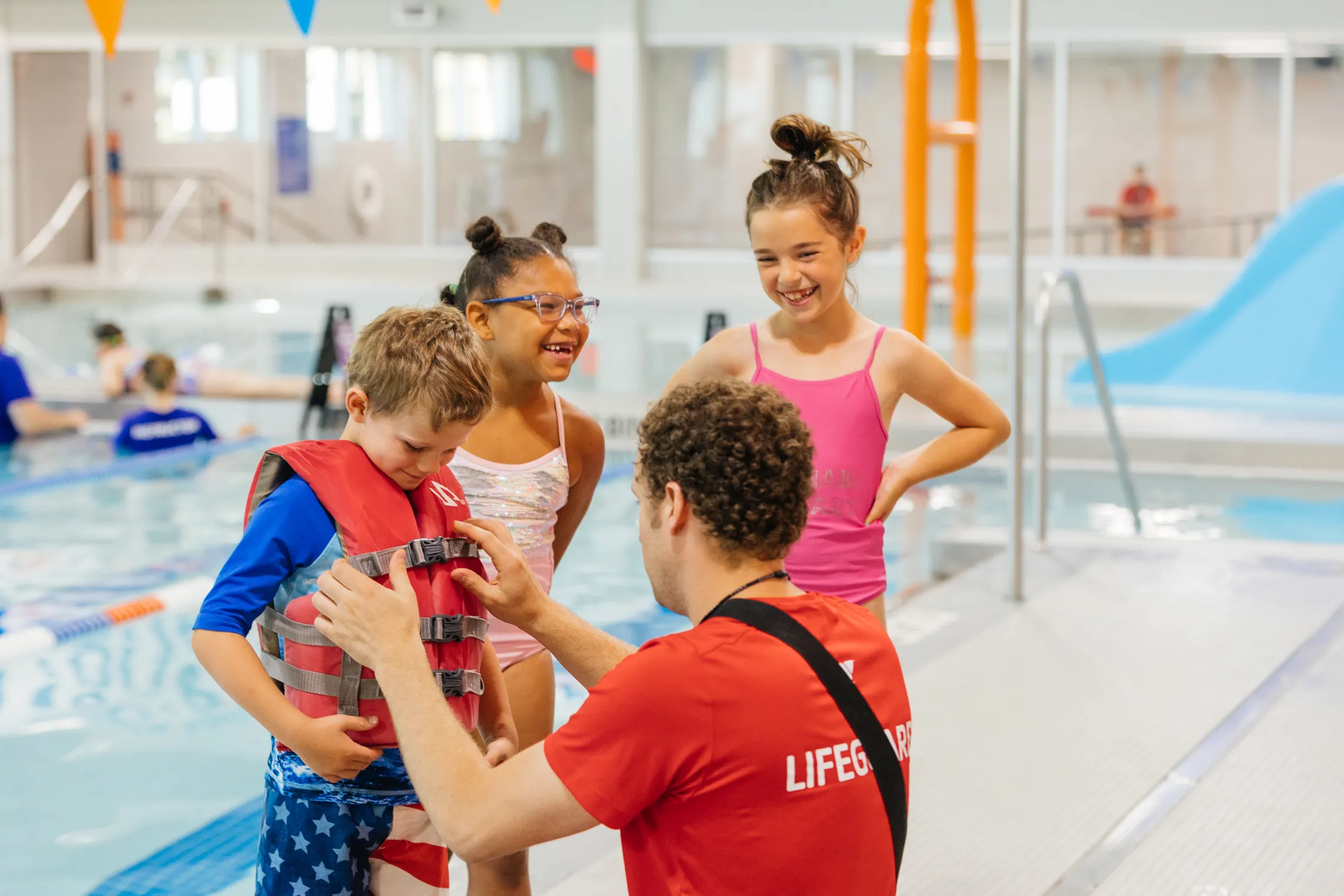 Image shows a lifeguard helping children put on a life vest on at the aquatics center at Fercho YMCA