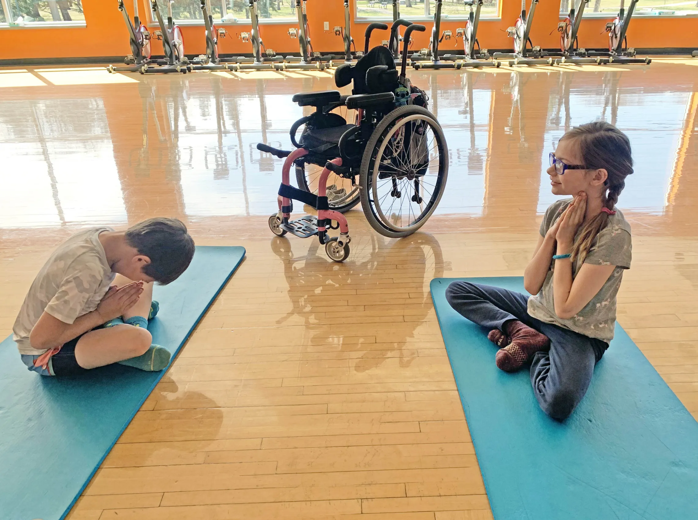Group of children with a wheelchair doing adaptive yoga in a group fitness room