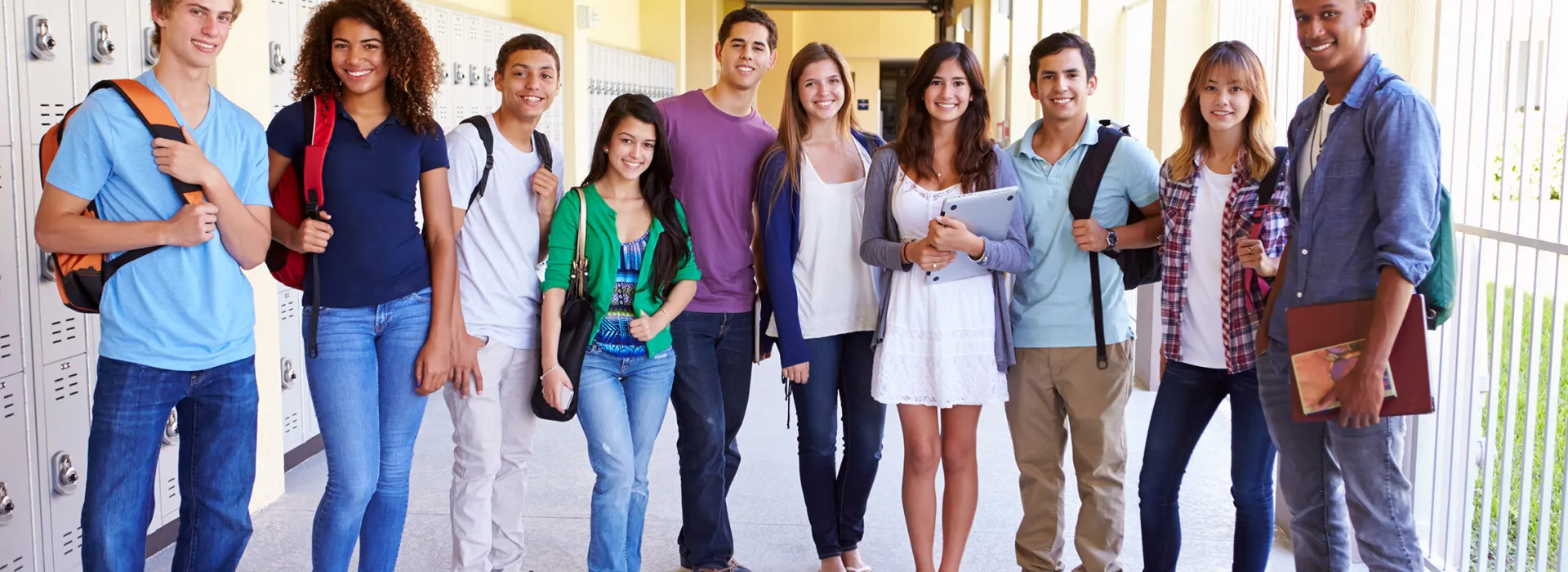 A group of 10 high schoolers in a yellow hallway smiling at the camera